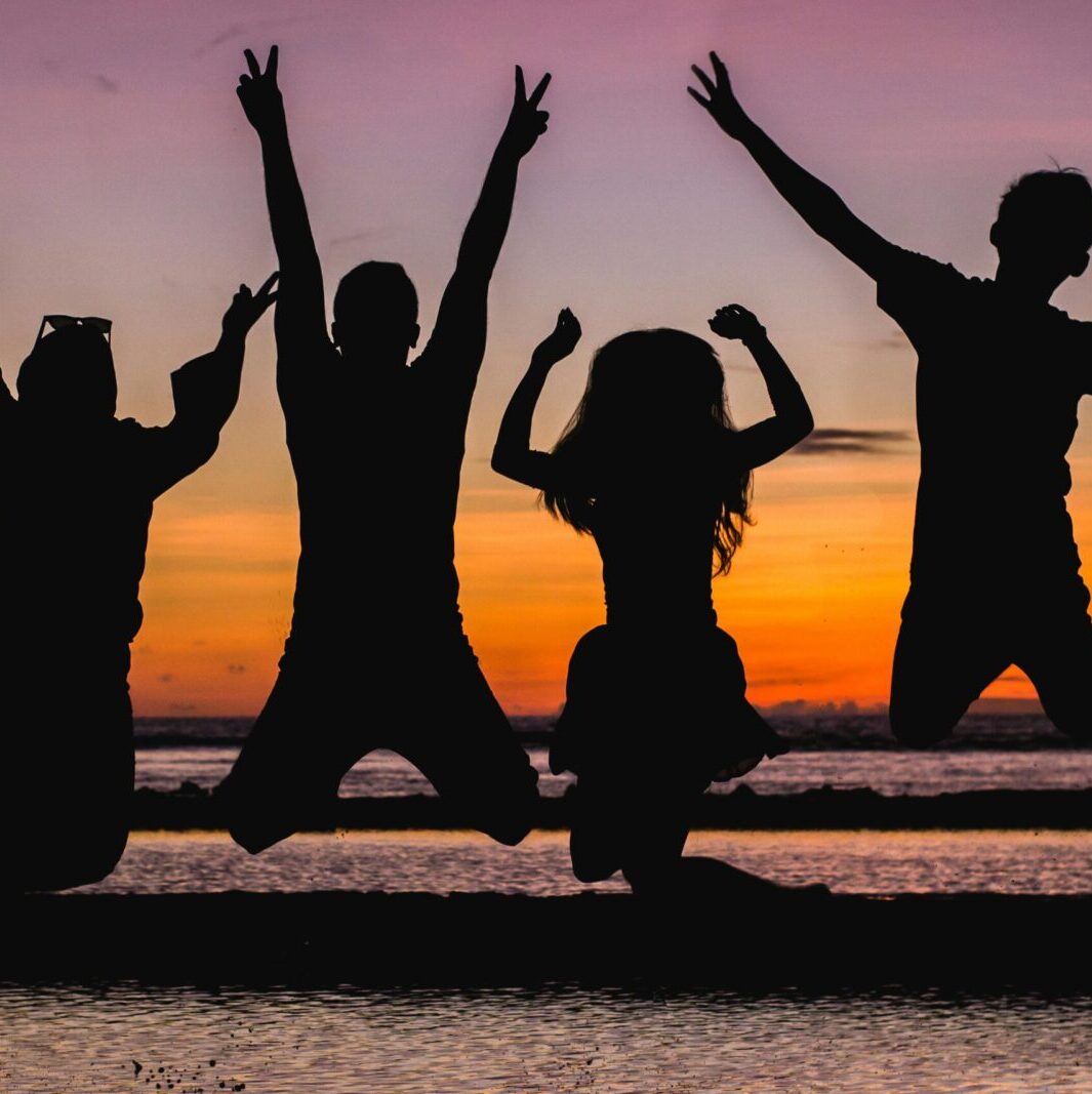 Silhouette of friends jumping on the beach at sunset, celebrating summer fun.
